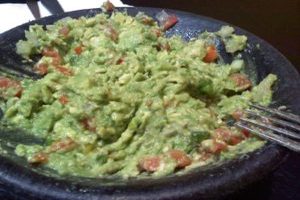 A bowl of guacamole with tomatoes and onions.