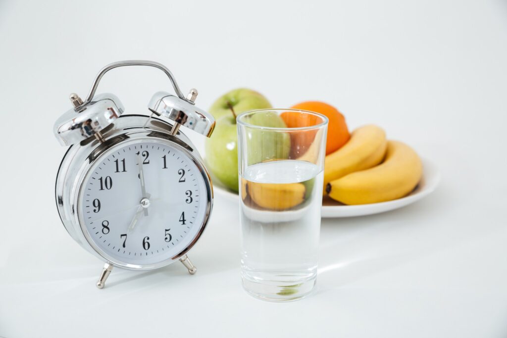 A clock and some fruit next to a glass of water