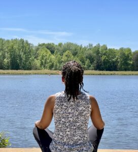 A woman sitting on the ground in front of water.